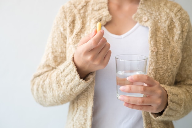 A woman holding a medicine and a glass of water in her hand. Medical and health concepts