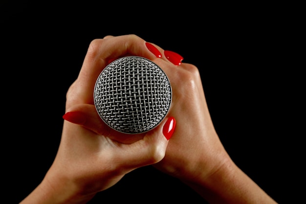 Woman holding microphone with two hands with red nails isolated on black background