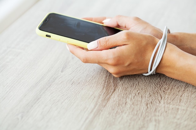 Woman holding mobile phone in hands tied with charging cable