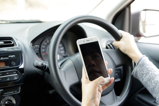 Woman holding mobile phone sending a text while driving a car.