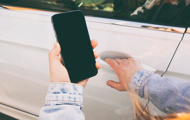 Woman holding mobile phone with blank screen next to door of her car in the street