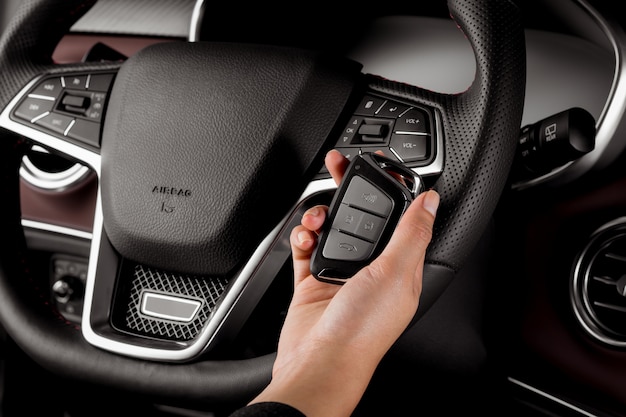 Woman holding modern car key, alarm system and steering wheel with electric buttons