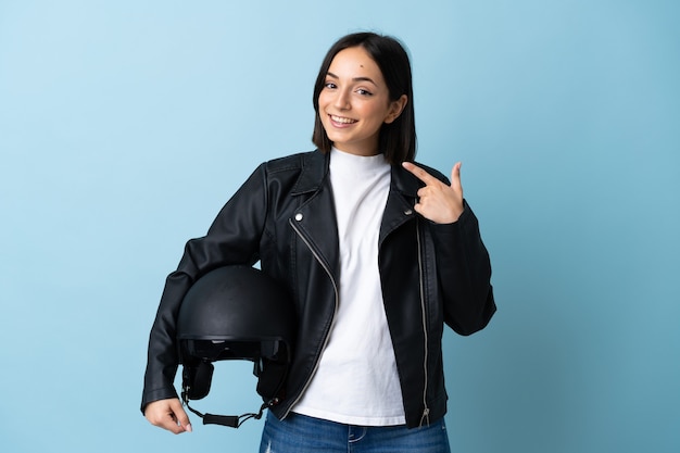 Woman holding a motorcycle helmet isolated on blue wall giving a thumbs up gesture