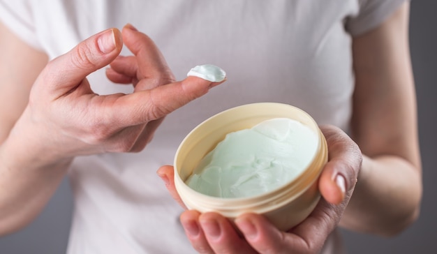 Woman holding an open jar of cream and taking the product on her finger