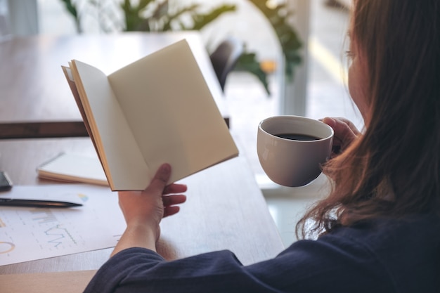 woman holding and opening a blank notebook while drinking coffee