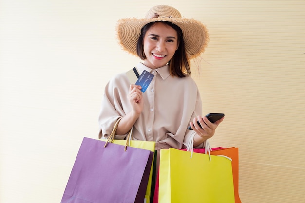 Woman holding paper bags and credit card with smile on yellow background in shopping concept