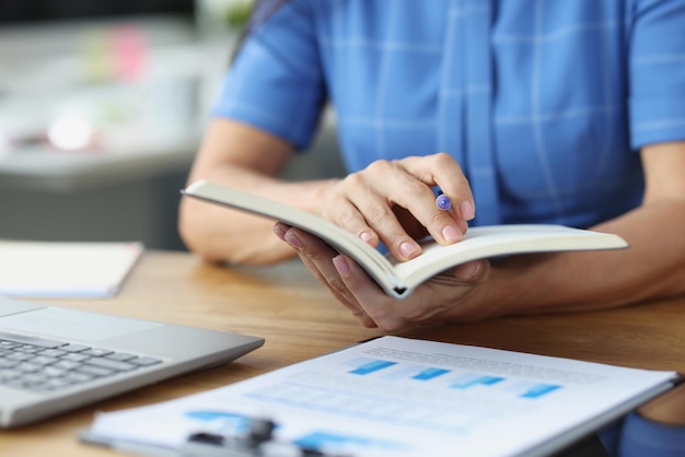 Woman holding pen and diary of our documents with charts closeup online business development