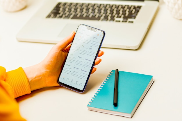 Woman holding phone and using calendar to make her plan in the notepad.