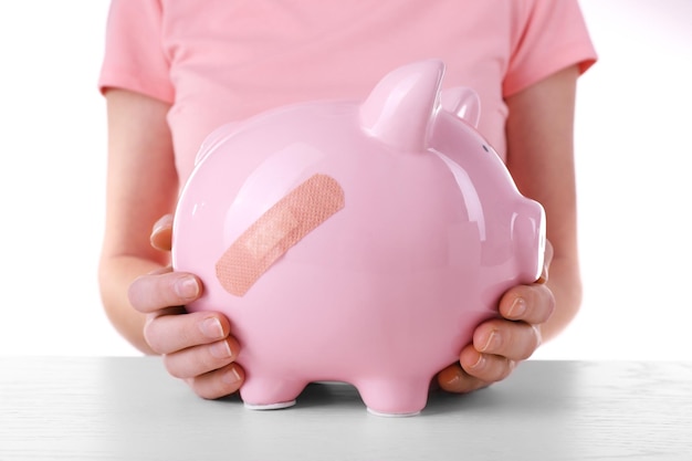 Woman holding Piggy Bank with adhesive bandage on white background