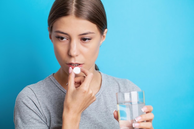 Woman holding pill and glass water taking medicine from headache stomach pain or taking vitamins