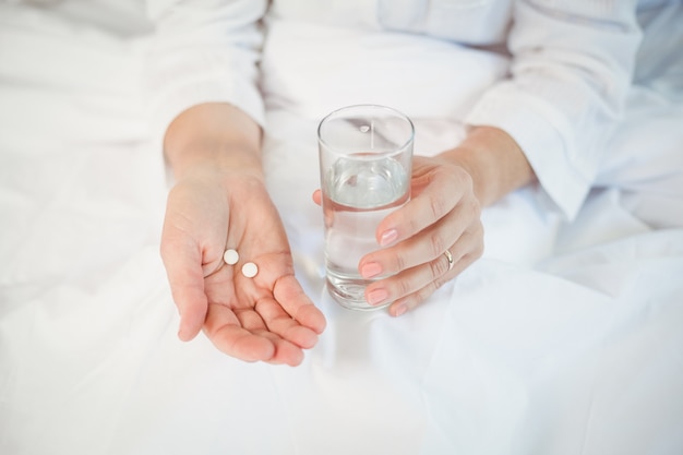 Woman holding pills and drinking glass