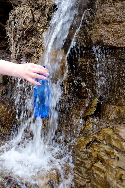 Woman holding a plastic bottle drawing clean water from cold spring