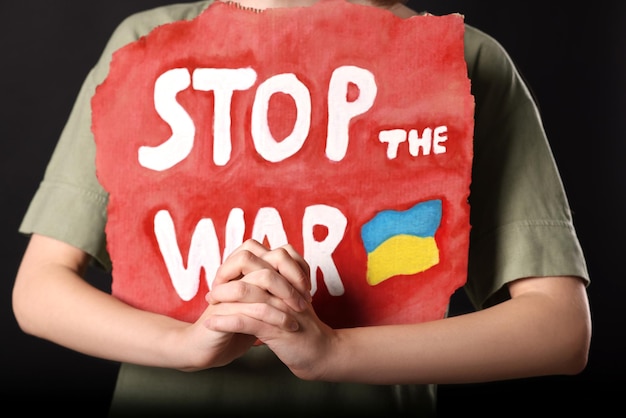 Woman holding poster with words Stop the War on black background closeup