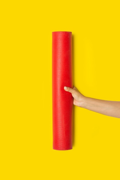 Woman holding a red yoga mat on a yellow background with copy space