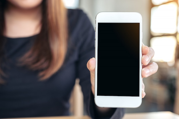 Woman holding and showing white mobile phone with blank screen