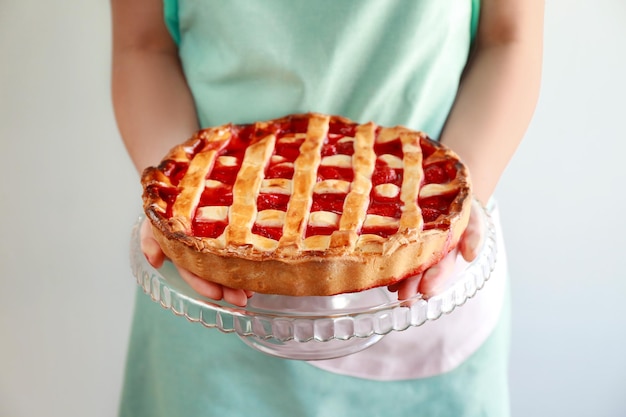 Woman holding stand with delicious strawberry cake on light background