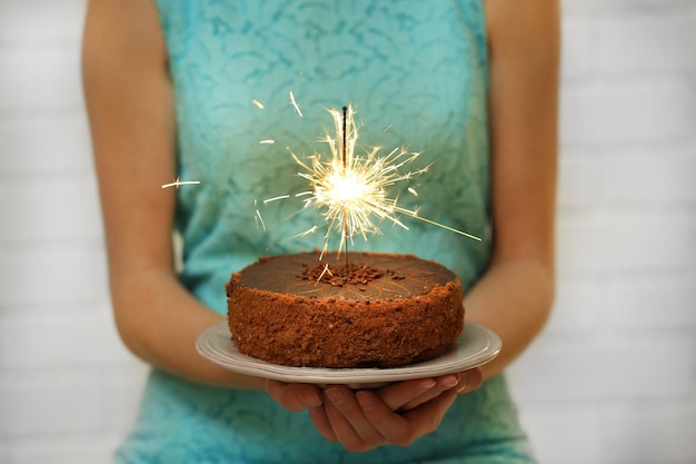 Woman holding tasty cake with sparkler on grey wall background