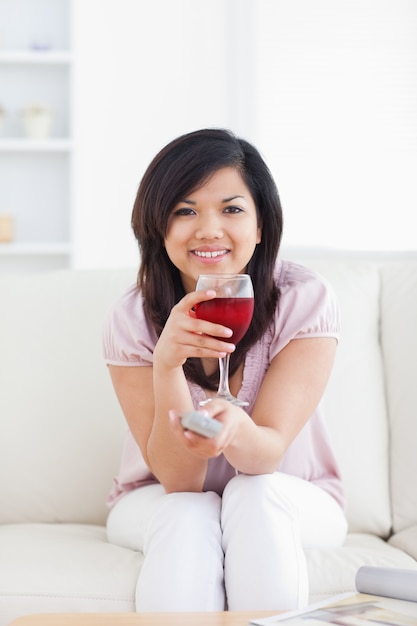 Woman holding a television remote while holding a glass of red wine