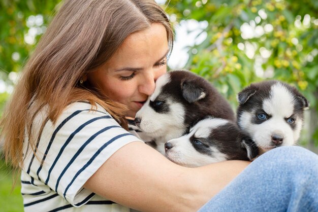 Woman holding three wonderful purebred husky puppies in her hands outdoors