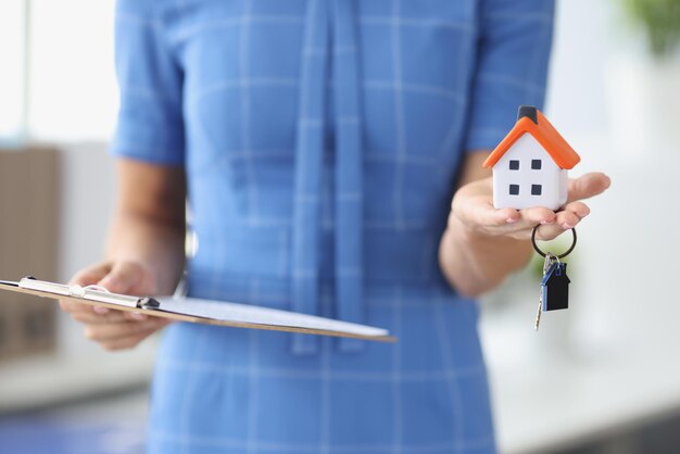 Woman holding toy house with keys and documents on clipboard closeup sale of residential real