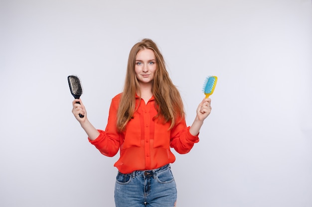 Photo woman holding two hairbrush posing with one half shaggy and combed hair medium shot