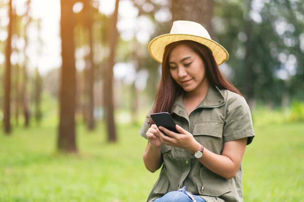 A woman holding and using mobile phone while sitting in the park