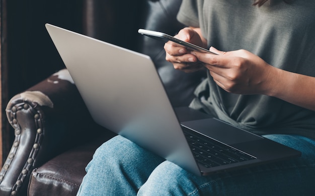 A woman holding and using mobile phone while working on laptop