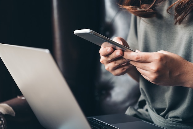 A woman holding and using mobile phone while working on laptop