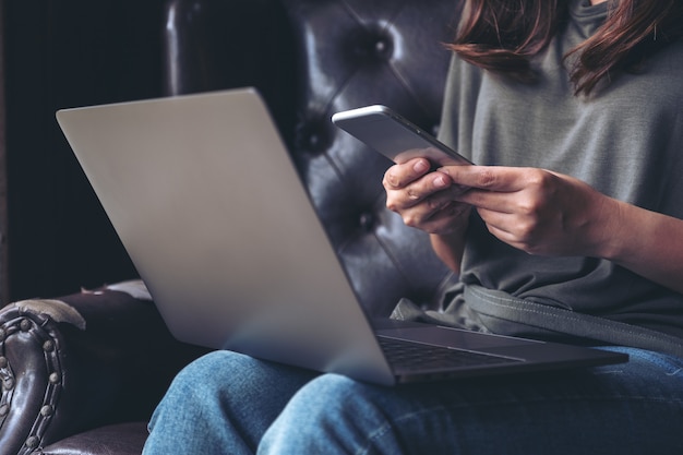 A woman holding and using a mobile phone while working on laptop