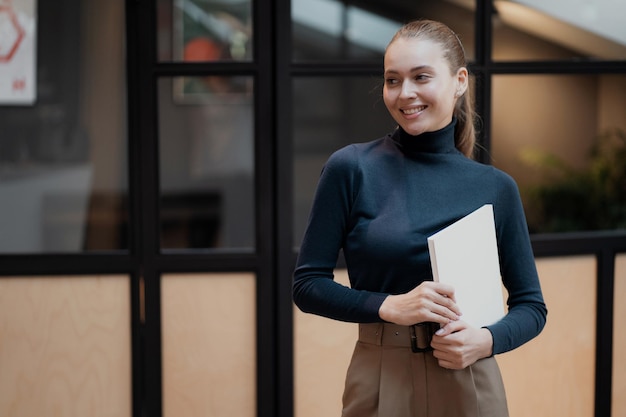 Woman holding a white book in her hands stands in the office and thinks about new