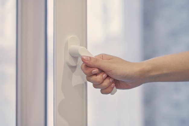 Woman holding white modern handle at PVC plastic window with double glazing, opening and closing frame. Close up.