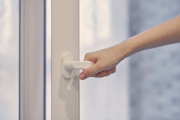 Woman holding white modern handle at PVC plastic window with double glazing, opening and closing frame. Close up.