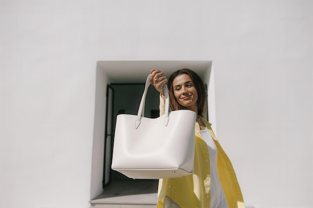 a woman holding a white purse with a yellow scarf on it