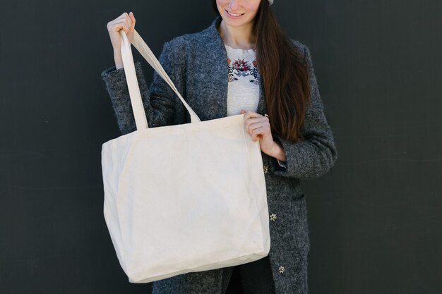 Woman holding white textile tote eco bag in urban area