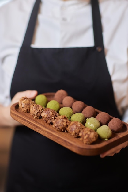 Woman holding wooden board with madeleine cookies at grey table closeup