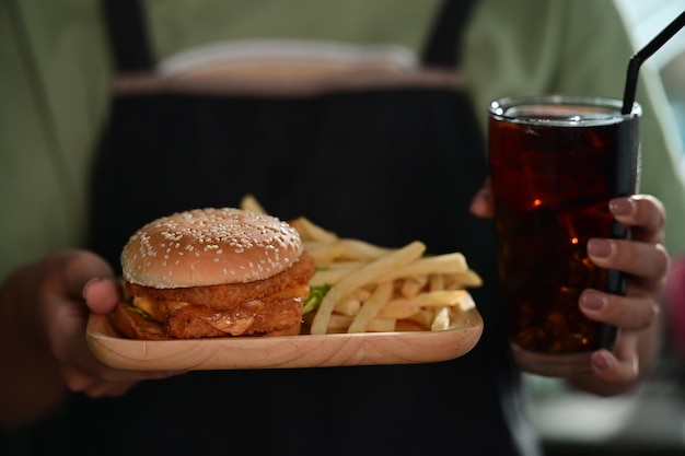 Woman holding wooden tray with delicious fish burger and glass of soft drink