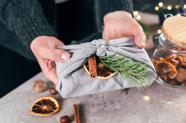 Woman holding wrapped gift in fabric with green branch, organic decoration. Zero waste christmas.