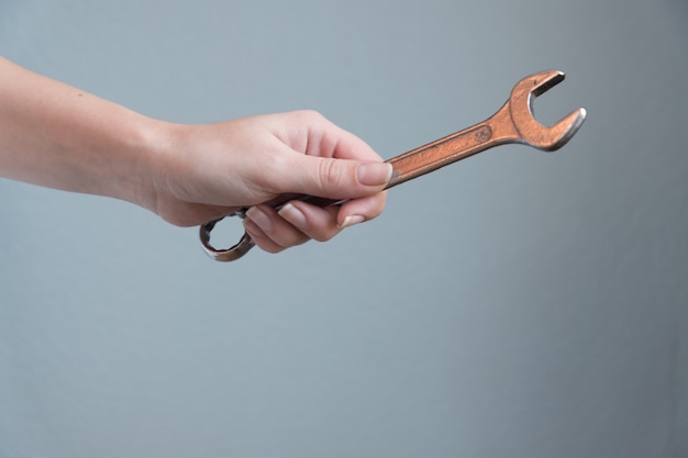 Woman holding a wrench in her hand on gray background.