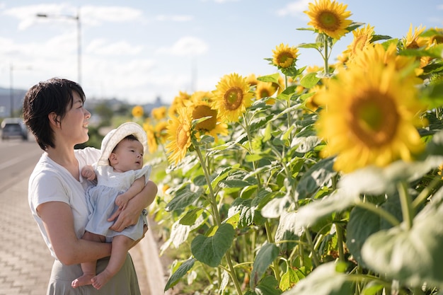 A woman holds a baby in a field of sunflowers.