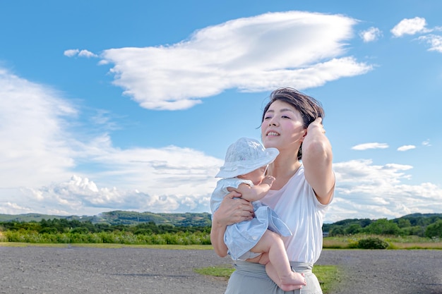 A woman holds a baby in her arms, looking up at a cloud in the sky.