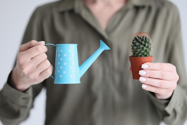 Woman holds blue watering can to water decorative green cactus with spines in hands female