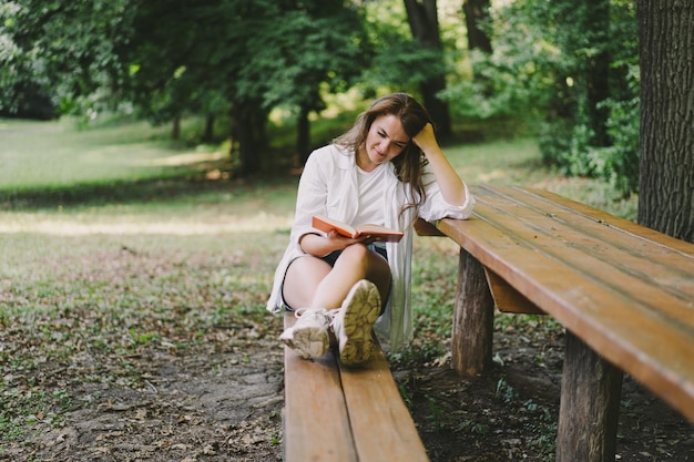 Photo woman holds book in her hands reading the book sitting on a bench at outdoors