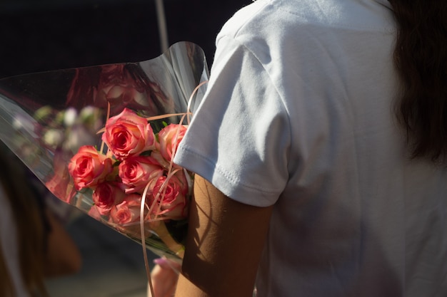 A woman holds a bouquet of red roses on her bent hand.