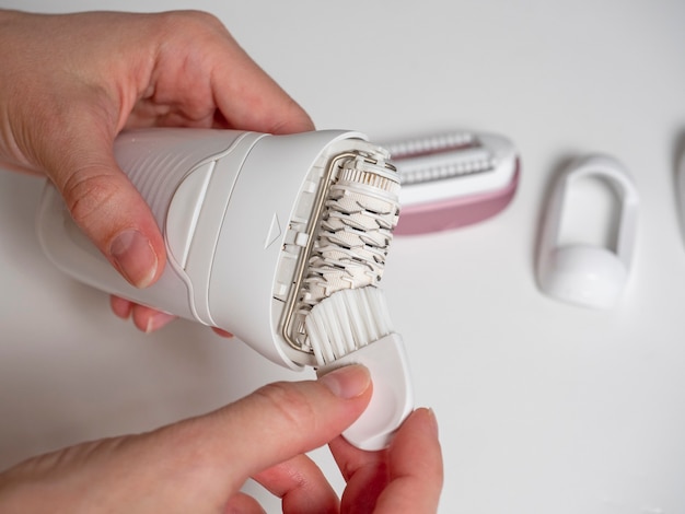 A woman holds and cleans an electric epilator with a brush on a white background. Maintenance of equipment