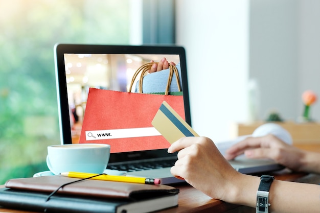 Woman holds credit card while uses laptop computer with shopping on line mock up.