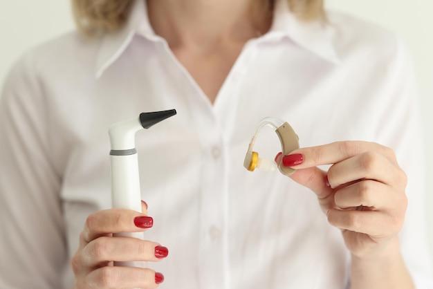 Woman holds digital otoscope and hearing aid in studio examining and treatment patient with