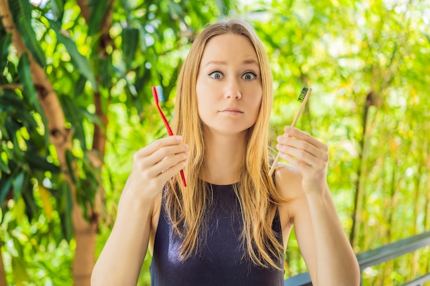 Woman holds eco natural bamboo toothbrush and in other hand plastic toothbrush rustic background sustainable lifestyle concept zero waste choice plastic free items