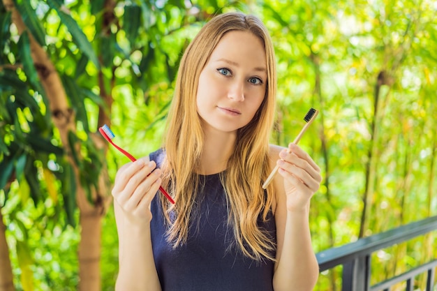 Woman holds eco natural bamboo toothbrush and in other hand plastic toothbrush rustic background sustainable lifestyle concept zero waste choice plastic free items