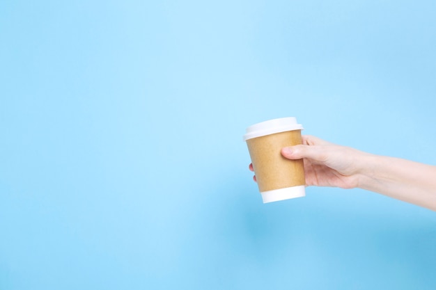 Woman holds hand paper cup with coffee on blue background. Copy space