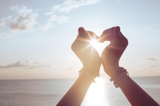 Woman holds hands up to sky in the shape of a heart around the sun